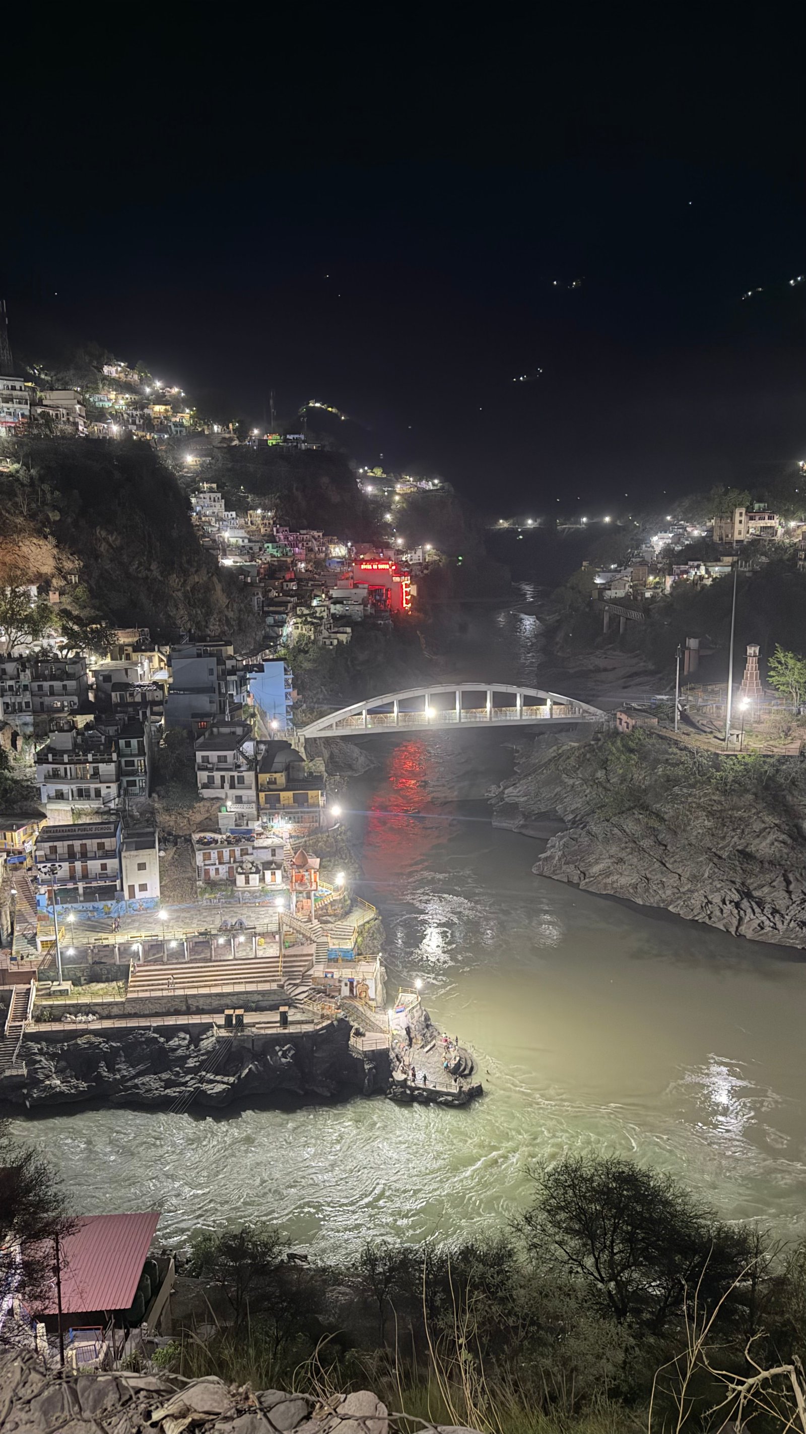 Night view of a river flowing through a hill town, illuminated by lights and connected by a bridge. 