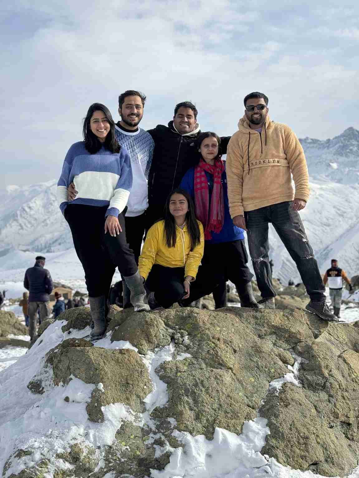 Five people posing on a snowy mountain viewpoint, with snow-covered peaks stretching across the background. 