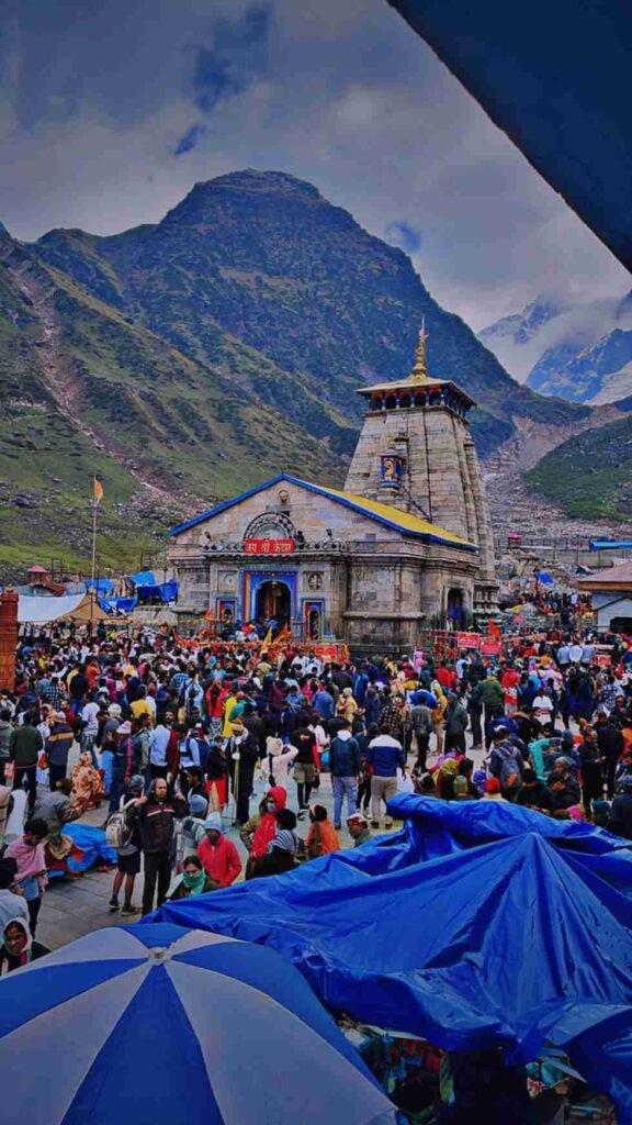 Pilgrims gathered at Kedarnath Temple, with the Himalayas rising in the background beneath cloudy skies.