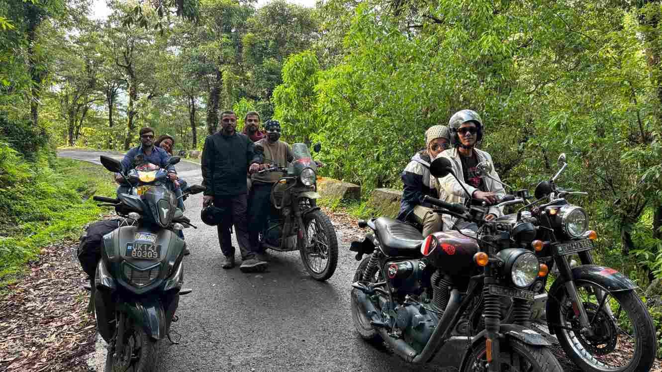 A group of riders posing with motorcycles on a scenic forest road surrounded by lush greenery. 