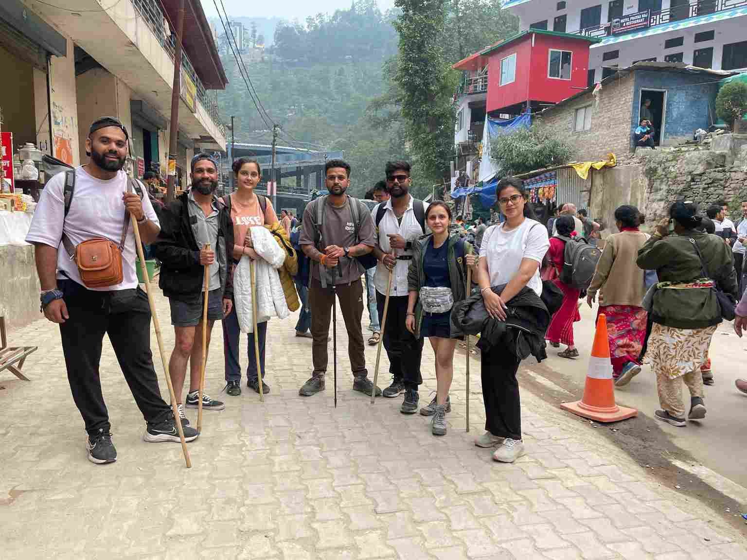 A group of trekkers posing with walking sticks in a bustling mountain town before beginning their journey. 